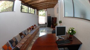 A long wooden table with a computer setup, two chairs, and a bench with colorful cushions.