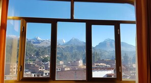 A view through a window with a mountain landscape, including snow-capped peaks and a town below. - Hotel Morales (Huaraz)