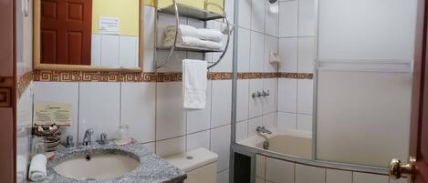 A bathroom with a sink, toilet, and shower. There is a towel rack with towels, a mirror, and a door.