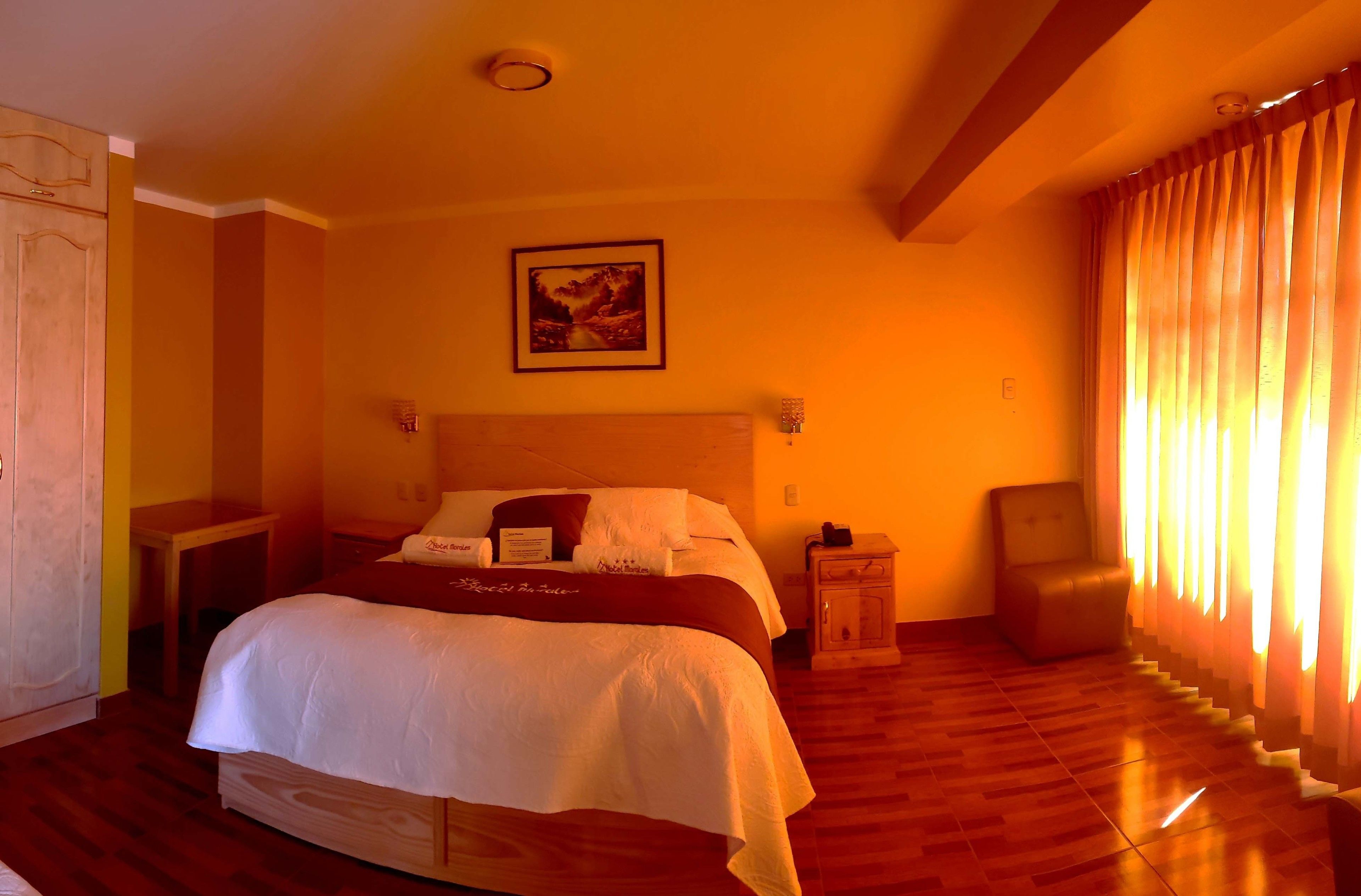 A hotel room with a large bed, a nightstand, a chair, and a window with curtains.