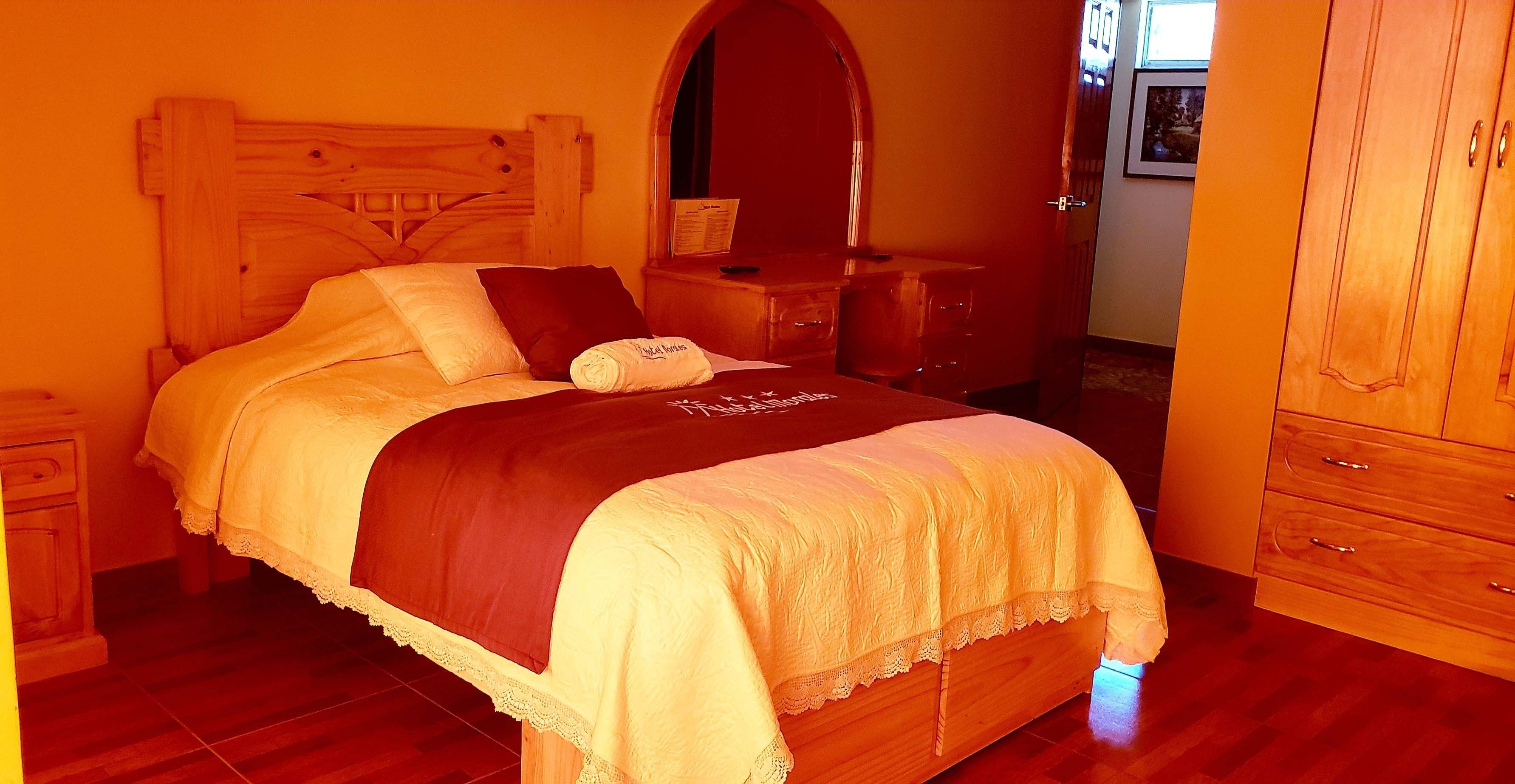 Una cama bien tendida con cabecera de madera, una mesita de noche con lámpara y un armario con cajones.