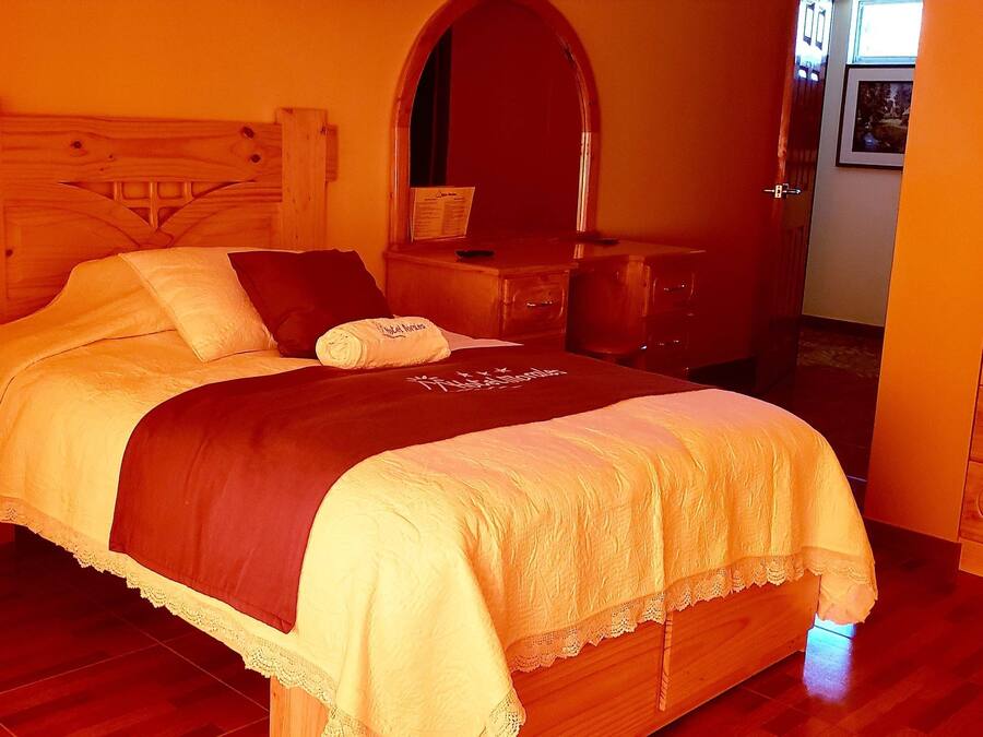 Una cama bien tendida con cabecera de madera, una mesita de noche con lámpara y un armario con cajones.