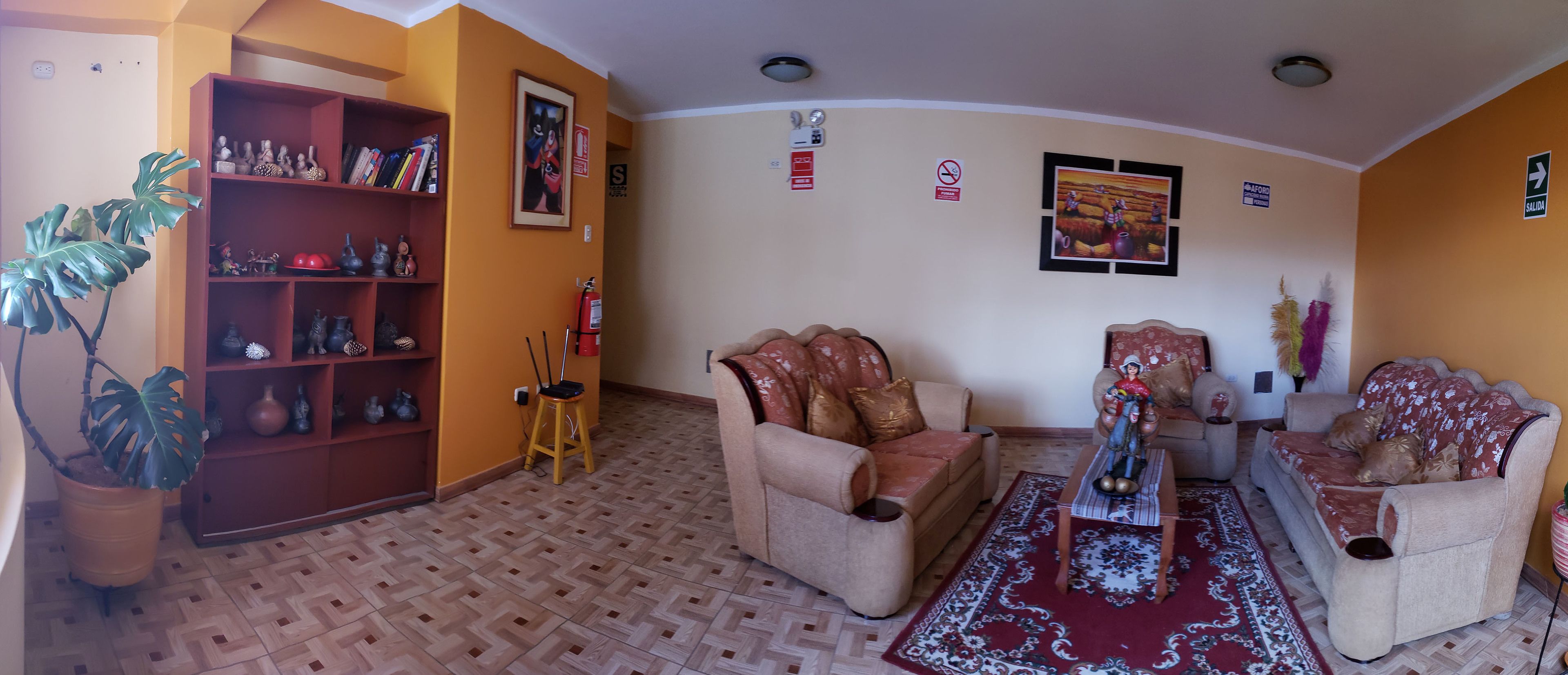 A living room with two beige armchairs, a coffee table, a bookshelf, a potted plant, and a patterned rug.