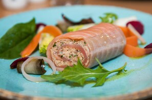 Une bouchée apéritive enroulée et farcie, entourée de divers légumes sur une assiette bleue.