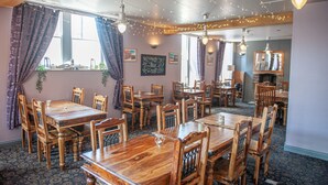 A restaurant interior with wooden tables and chairs, string lights, and a chalkboard menu on the wall.