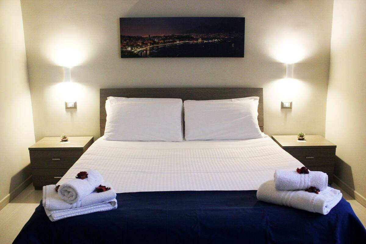A hotel room with a large bed, two bedside tables, and a night view painting.