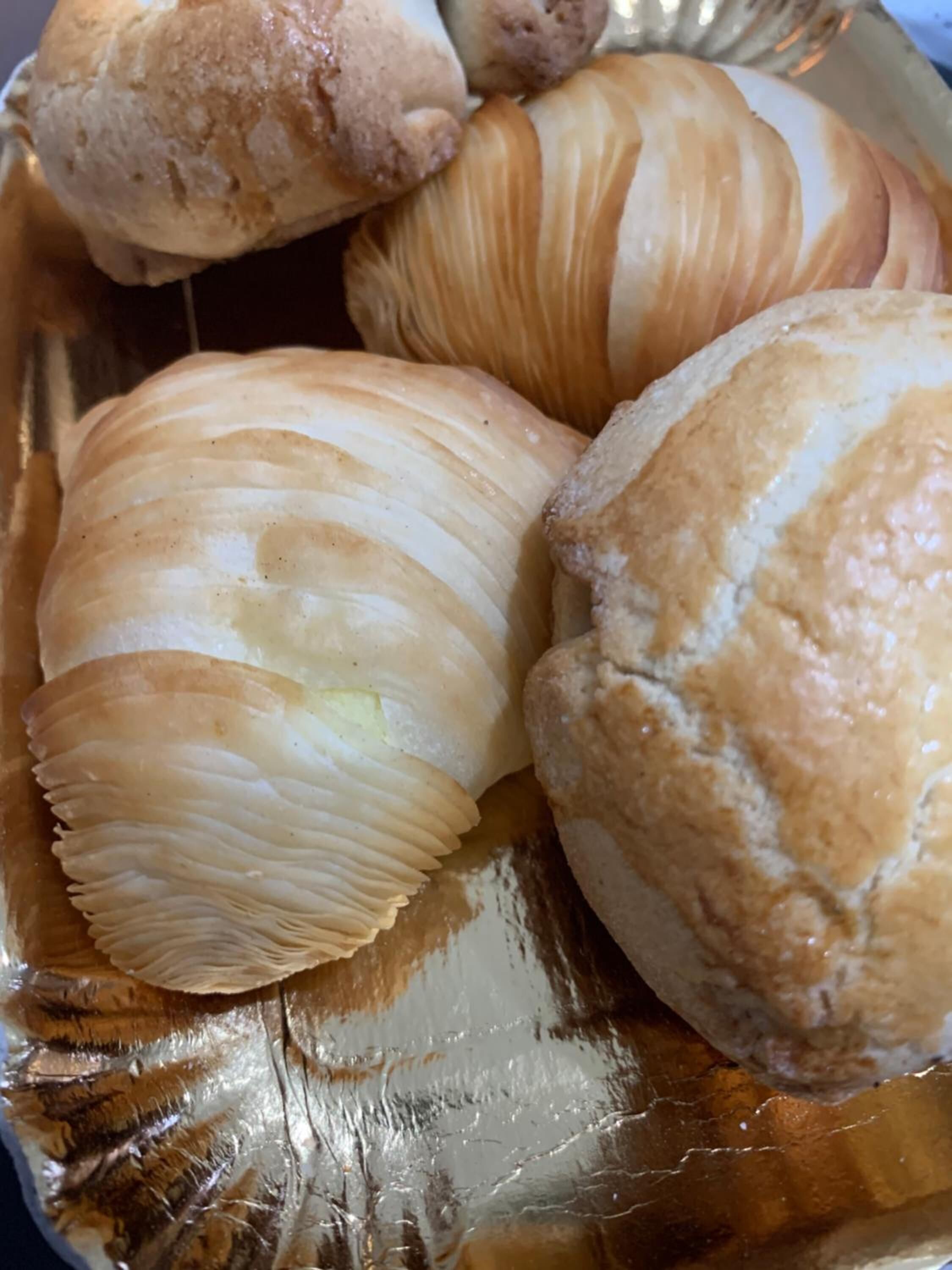 A tray of golden-brown pastries with a flaky texture, likely croissants, arranged on a reflective surface.