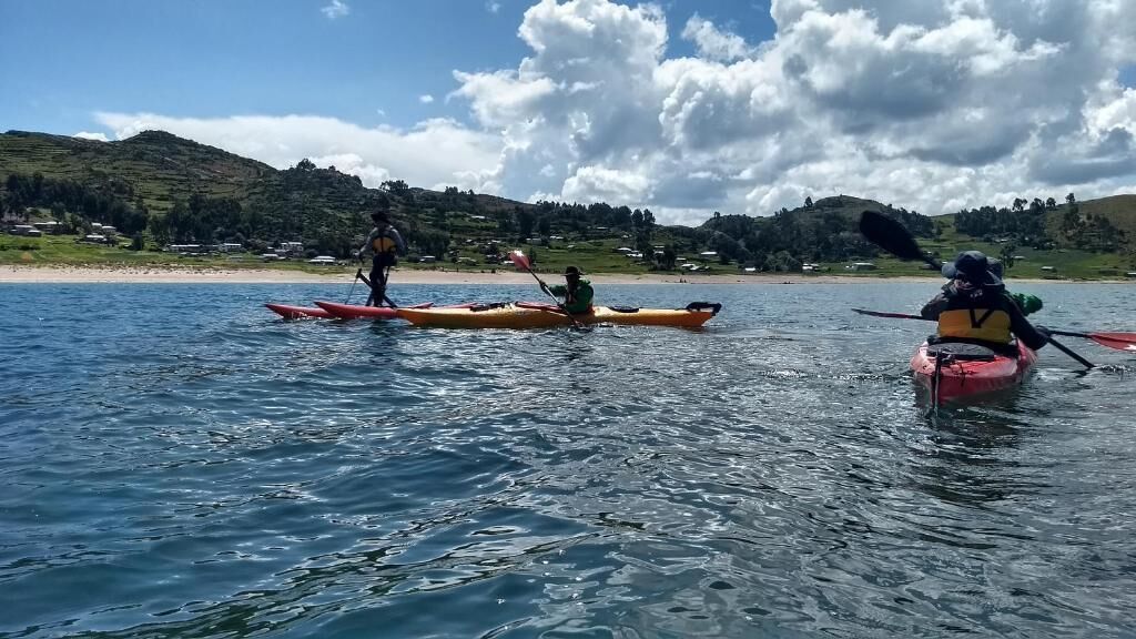 Three kayaks on calm water with a hilly landscape in the background.