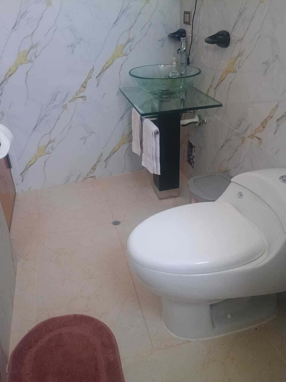 A bathroom with a glass sink, a toilet, and a marble-patterned wall.