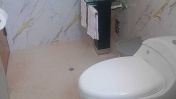 A bathroom with a glass sink, a toilet, and a marble-patterned wall.
