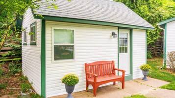 A small, single-story building with a green trim, a bench, and two potted plants.