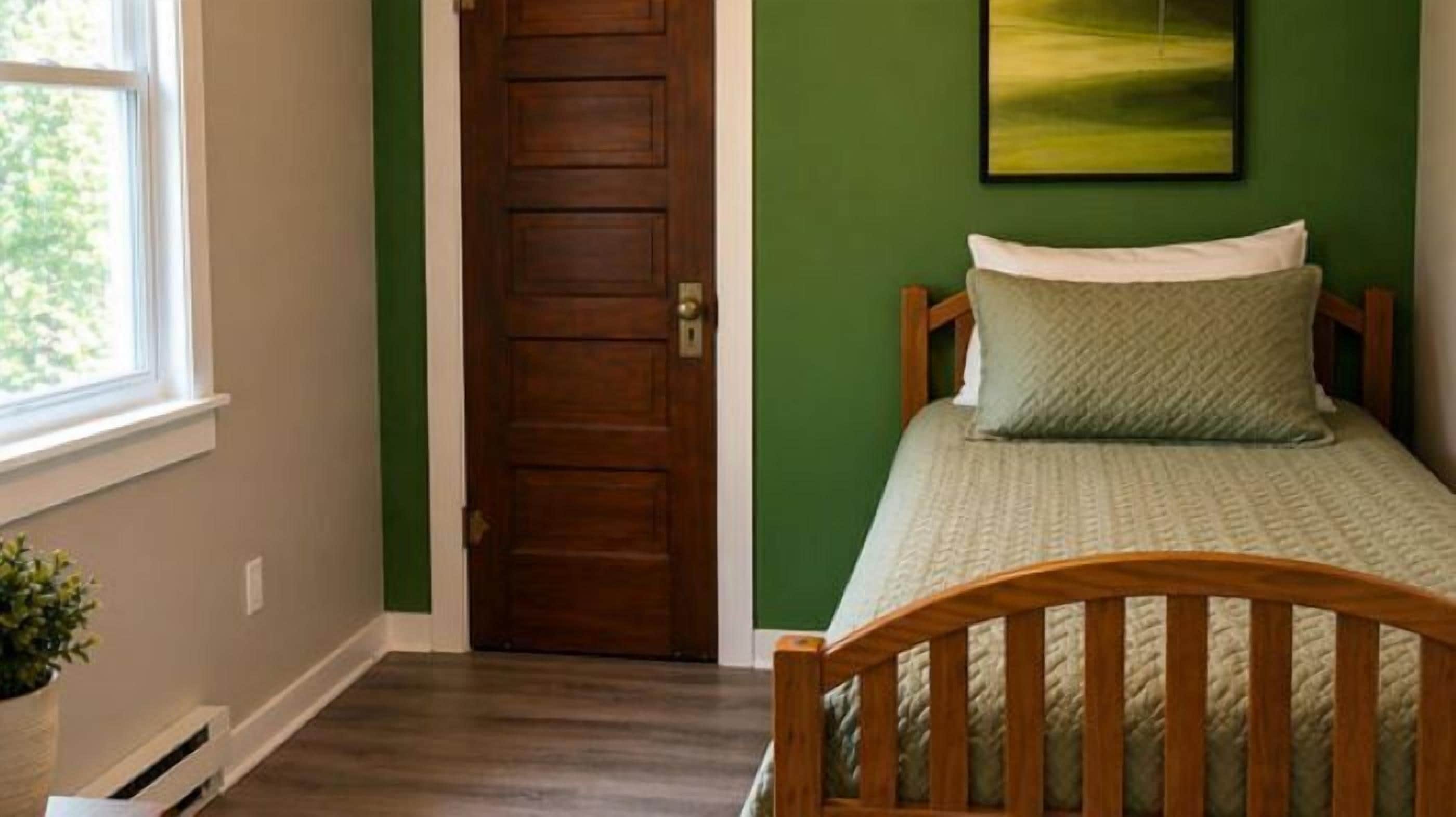 A room with a wooden door, a bed with a headboard, a window, and a green wall.