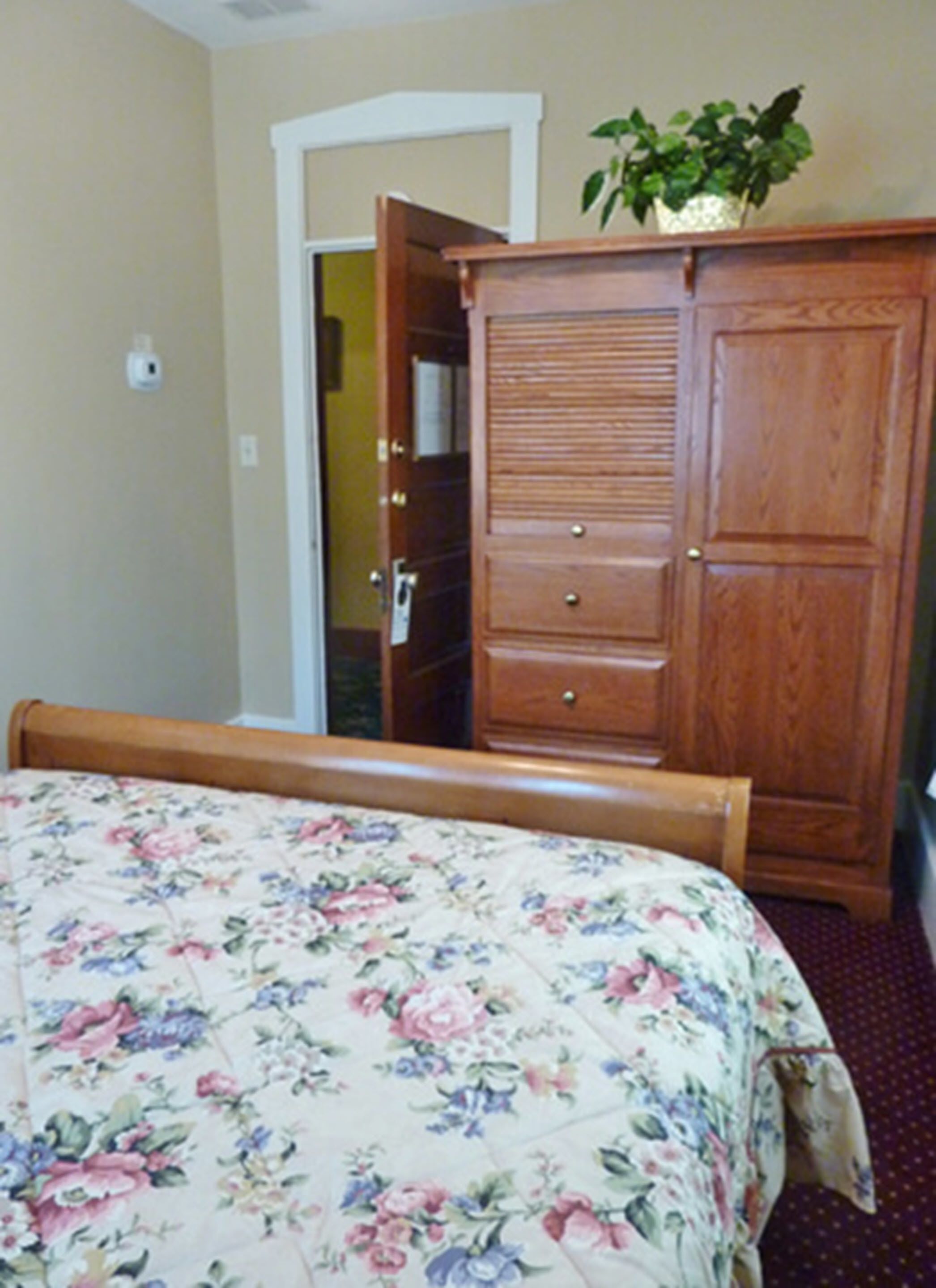 A bedroom with a bed, a wooden dresser, and a door leading to another room.