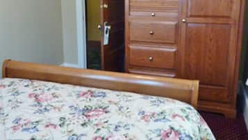 A bedroom with a bed, a wooden dresser, and a door leading to another room.