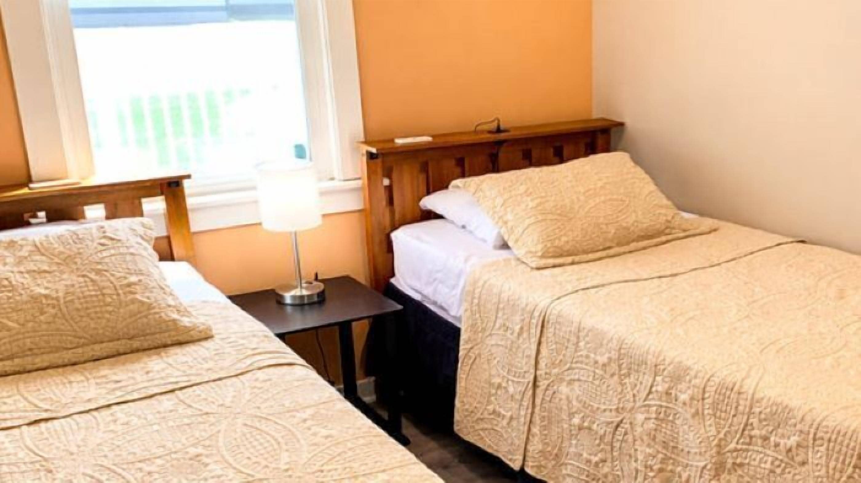 A room with two beds, a nightstand, a lamp, and a window with a view.