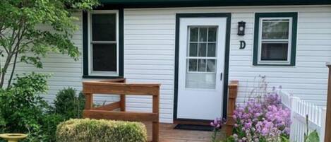 A white building with a green roof, a front door, and a small porch with a bench.