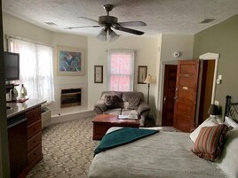 Ein Schlafzimmer mit Bett, einer Couch, einem Fernseher, einem Kamin und einem Deckenventilator.