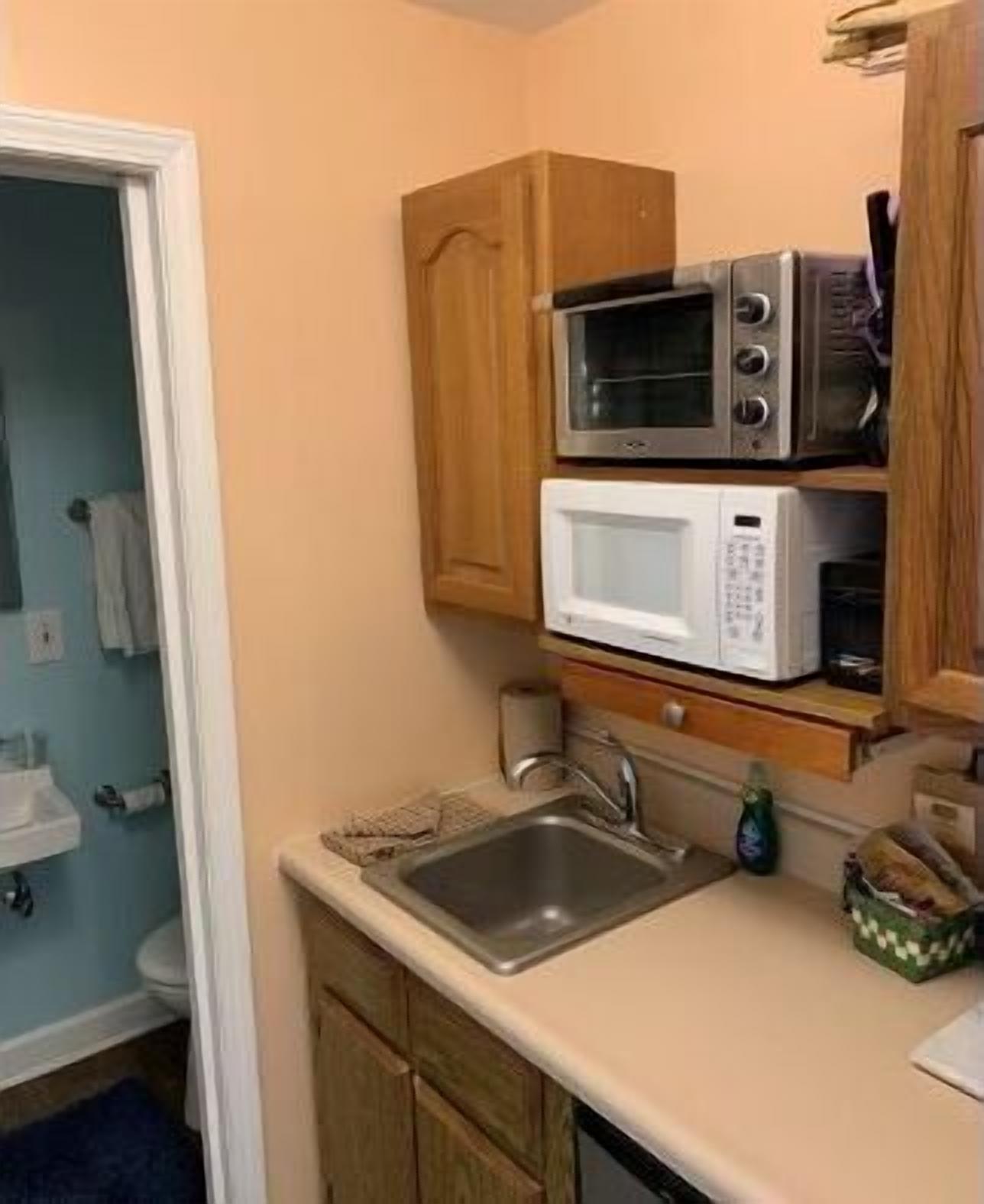 Une cuisine de taille réduite, équipée d’un évier, de deux micro-ondes et de meubles de rangement en bois.