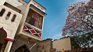 Un edificio tradicional con un balcón, arcos de piedra y un árbol con flores rosadas.
