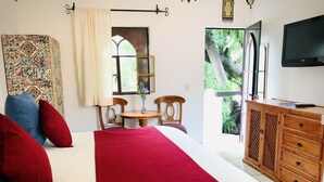 Un dormitorio con cama, cómoda de madera, televisión, ventana y vista a zonas verdes.