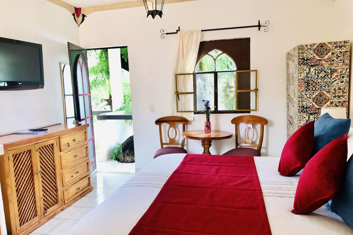 Una habitación con cama, escritorio de madera, televisor, ventana con cortinas y pared con diseño.
