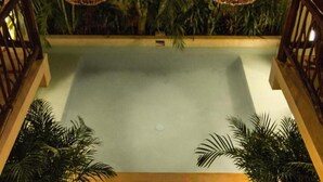 Una zona de piscina con dos lámparas colgantes de mimbre, rodeada de plantas en macetas y una barandilla de madera.