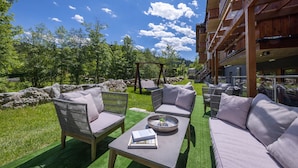 An outdoor seating area with wicker furniture and a table, surrounded by a lush green lawn and trees.