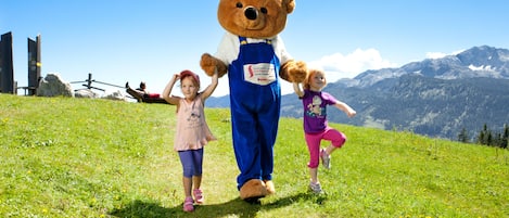 A large teddy bear mascot on a grassy field with mountains in the background.