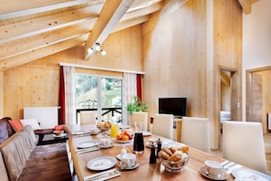 A wooden interior with a dining table set for breakfast, a sofa, and a TV in the background. - Apart- and Wellness Hotel Garni Dachsteinresort (Russbach am Pass Gschuett)