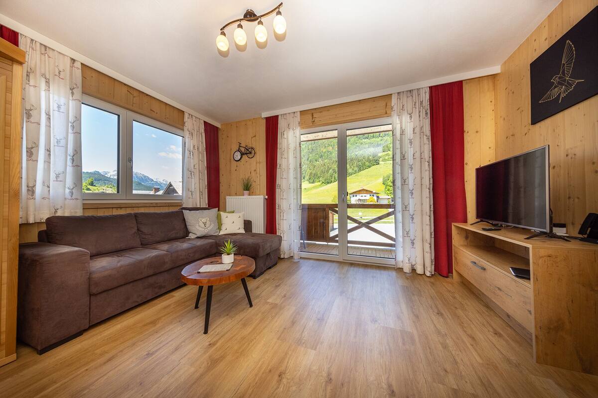 Uma sala de estar acolhedora com um sofá marrom, uma mesinha de centro de madeira e uma televisão sobre um móvel de madeira.