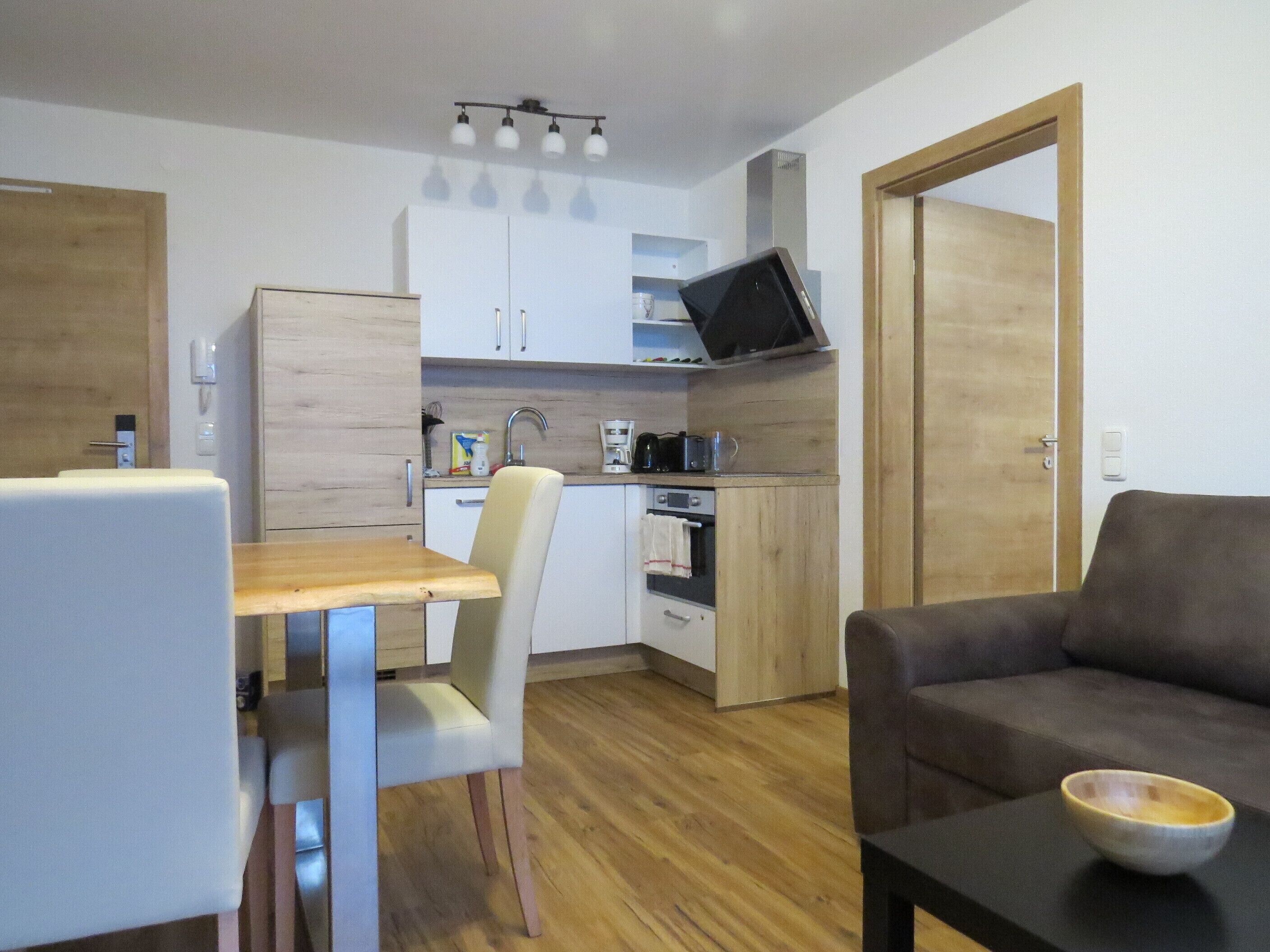A compact living space with a kitchenette, a dining area with a table and chairs, a sofa, and a television mounted above the counter.