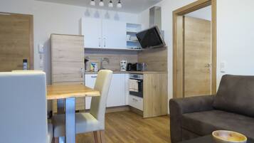 A compact living space with a kitchenette, a dining area with a table and chairs, a sofa, and a television mounted above the counter.