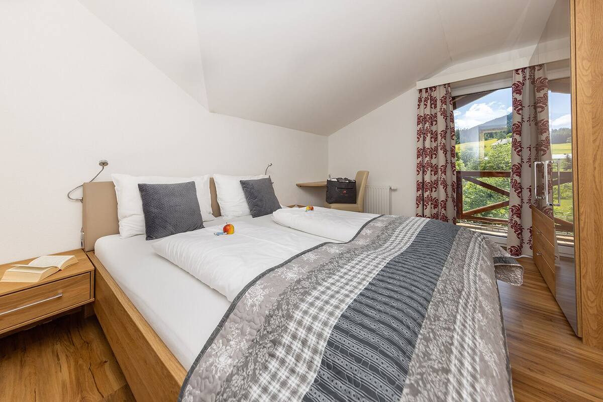 Quarto com uma cama grande, mesa de cabeceira, cômoda e vista para o exterior.