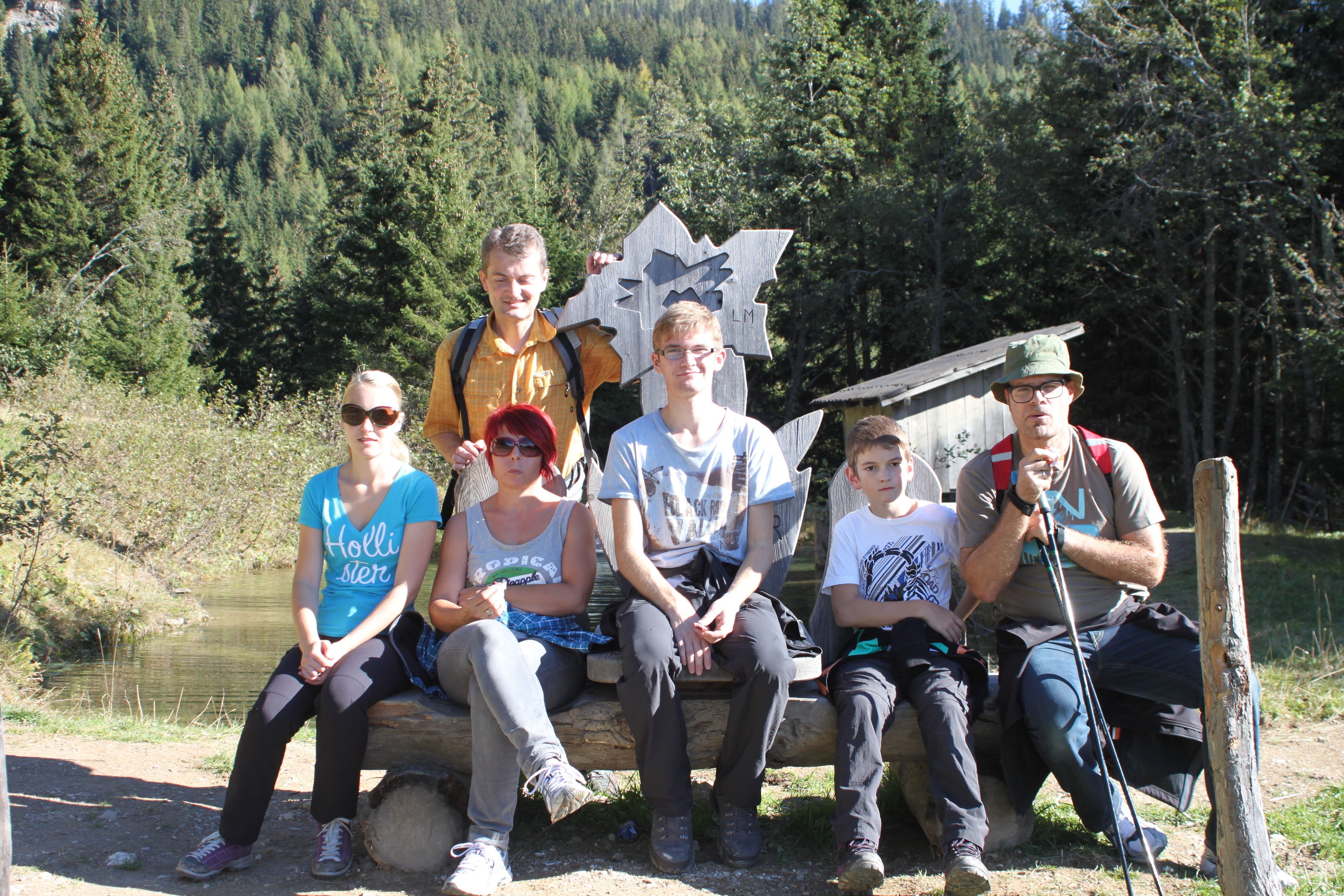 Un groupe de personnes est assis sur un banc à l’extérieur, avec une forêt en arrière-plan.