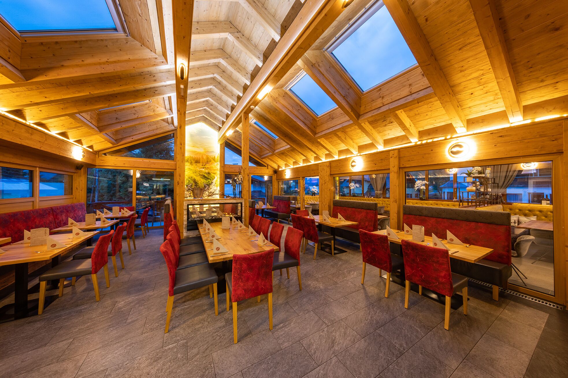 A restaurant with wooden beams and skylights, red upholstered booths, and a tiled floor.