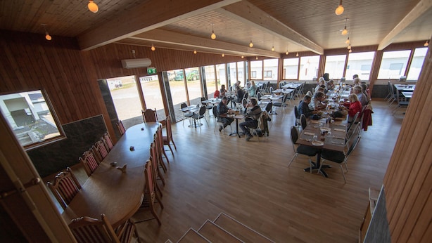 A spacious dining area with wooden tables and chairs, large windows, and hanging lights. - Hotel Breidavik (Vesturbyggð)