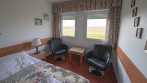 A hotel room with a bed, two chairs, a small table, and a window with curtains. - Hotel Breidavik (Vesturbyggð)