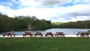 En picknickplats vid sjön med träbord och en stuga i bakgrunden.