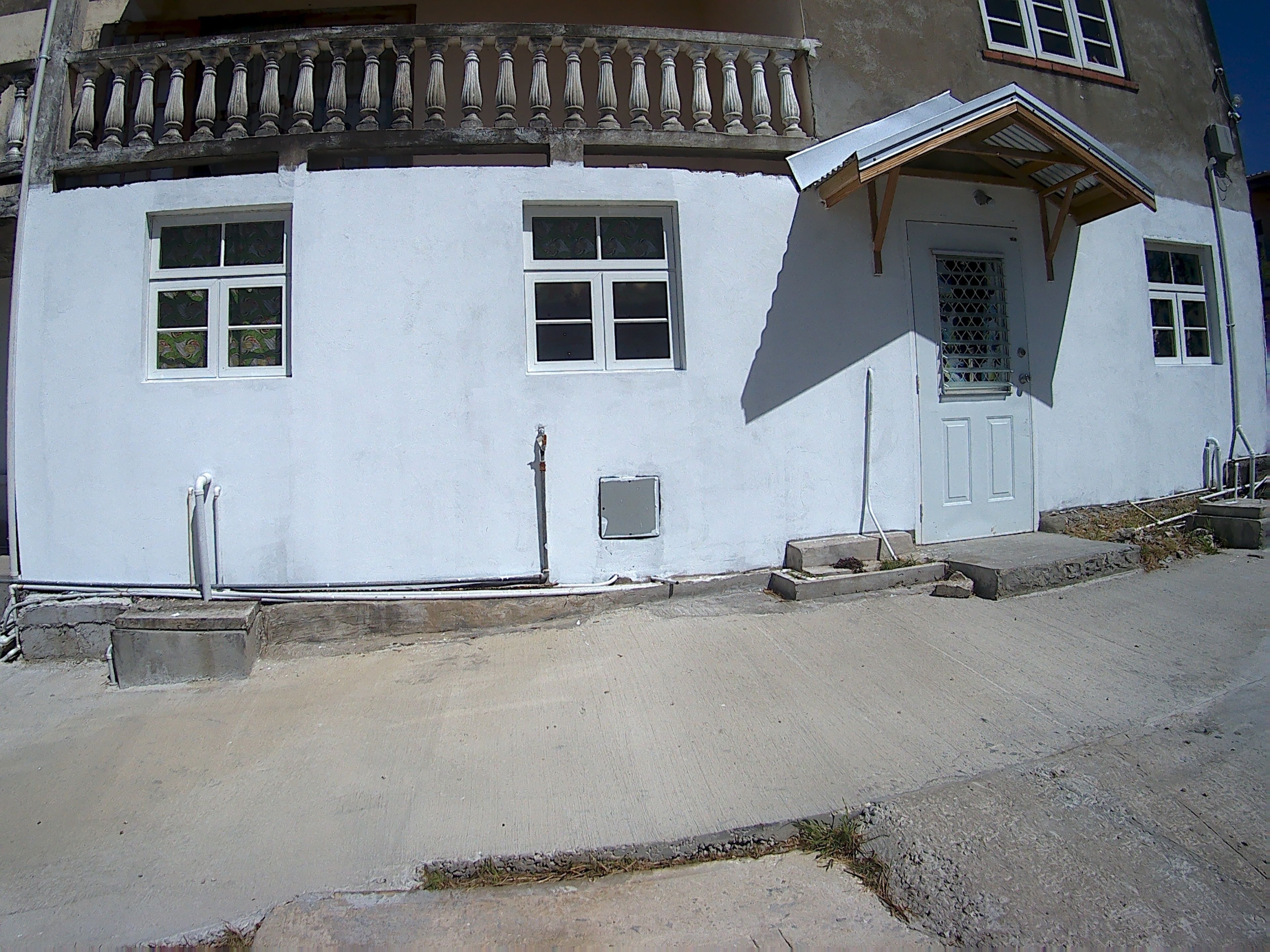 A white building with a balcony, a door with a metal gate, and a small window.