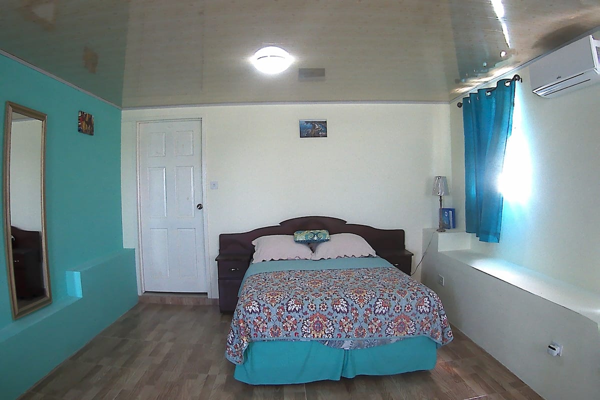 A bedroom with a bed, a door, a mirror, and a window with curtains.