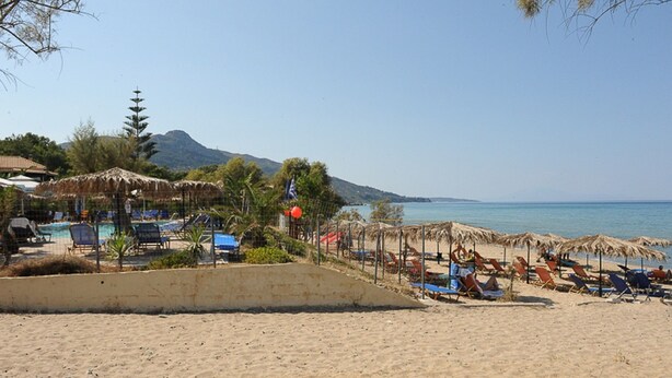 Een strand met ligbedden, parasols en een zwembad.