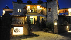 Een gebouw van steen met een balkon op de tweede verdieping, een garage met een auto en een goed verlichte ingang.