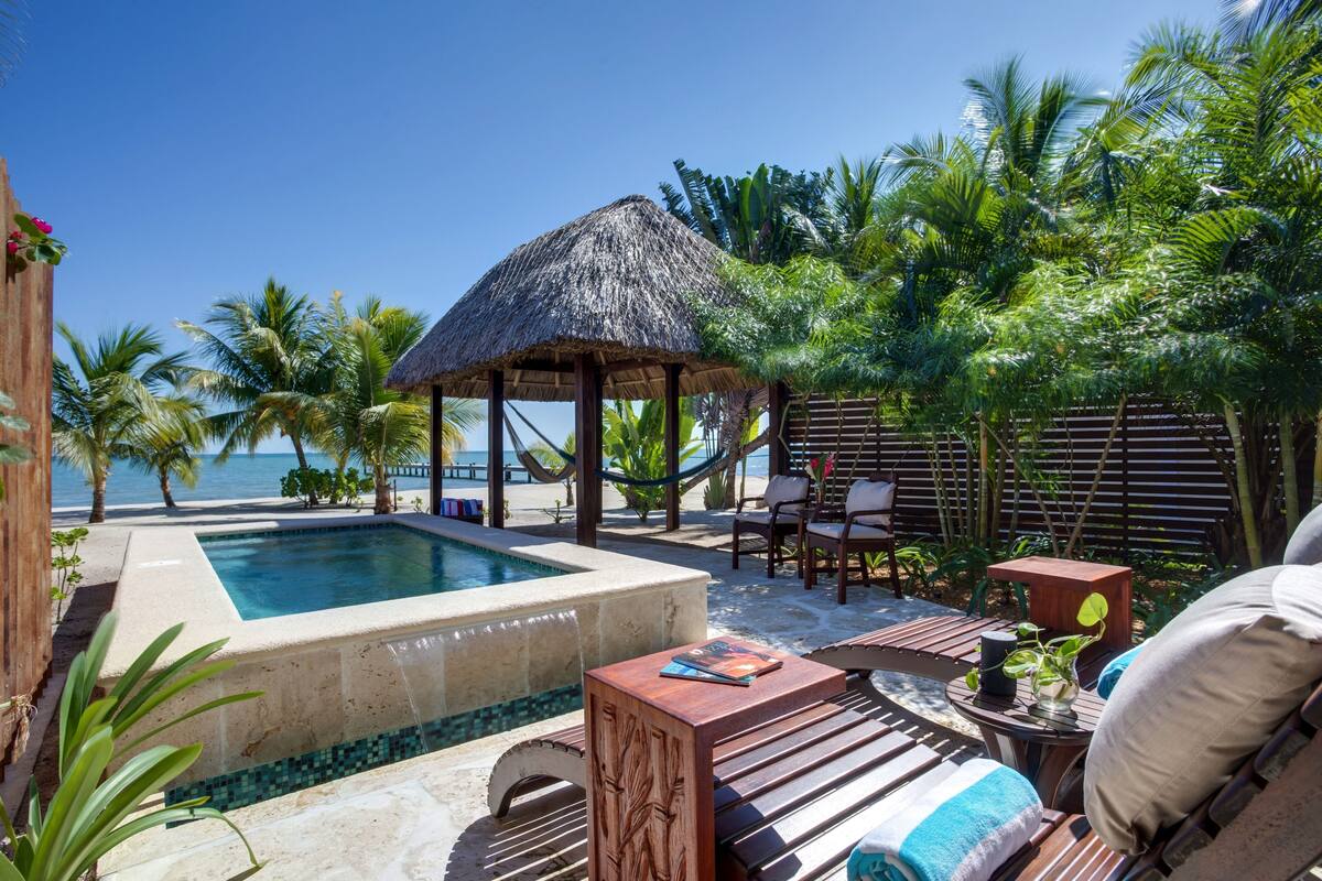 Ein Poolbereich mit einer strohgedeckten Struktur, Liegestühlen und Blick aufs Meer.