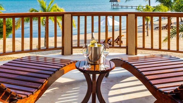 Une terrasse en bois avec une table et des chaises, donnant sur une plage bordée de palmiers et sur une jetée.