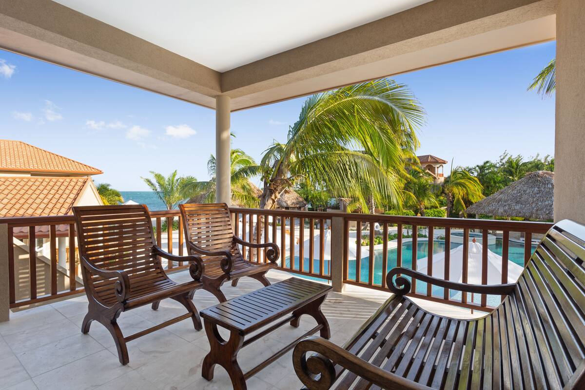 Ein überdachter Außenbereich mit Holzmöbeln, einem Pool und Blick auf das Meer und Palmen.