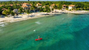 Une station balnéaire dotée de villas en bord de mer, d’eaux turquoise cristallines et où l’on peut voir une personne faire du paddle.