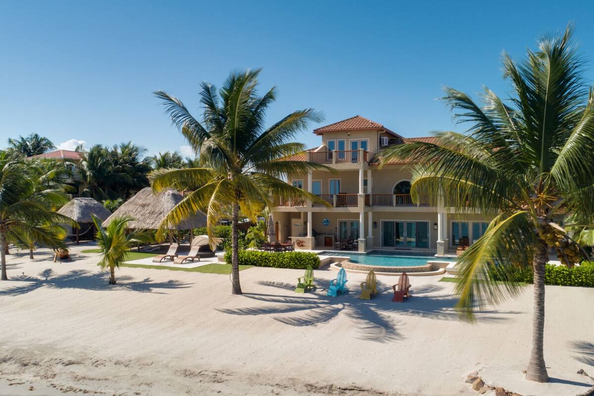 Ein Strandhotel mit Schwimmbad, Palmen und einer Struktur mit Reetdach.
