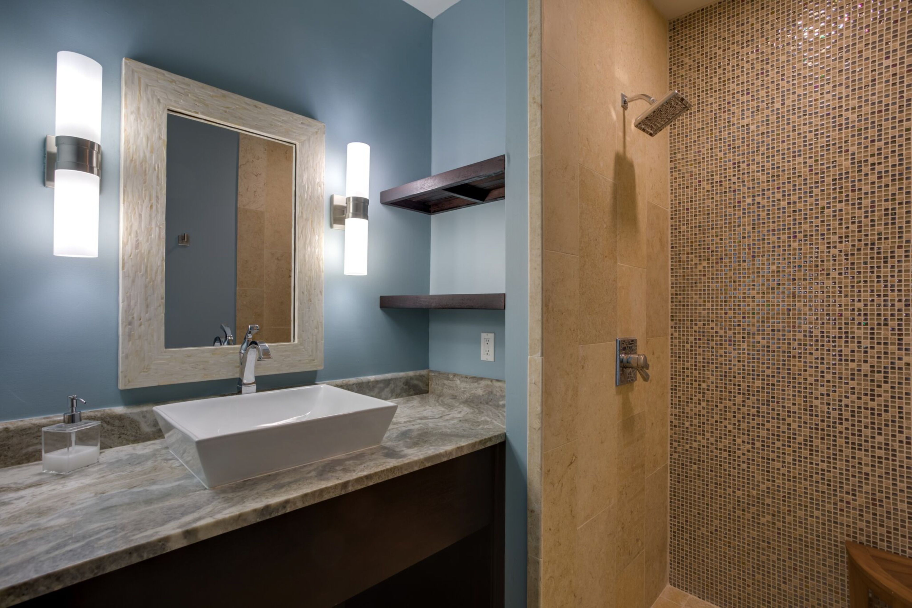 A bathroom with a large white sink, a mirror, and a shower with mosaic tiles.