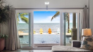 Une pièce dotée d’une grande porte-fenêtre coulissante donnant sur la plage, d’une plante en pot, d’un canapé agrémenté d’un coussin à motifs et d’une lampe.