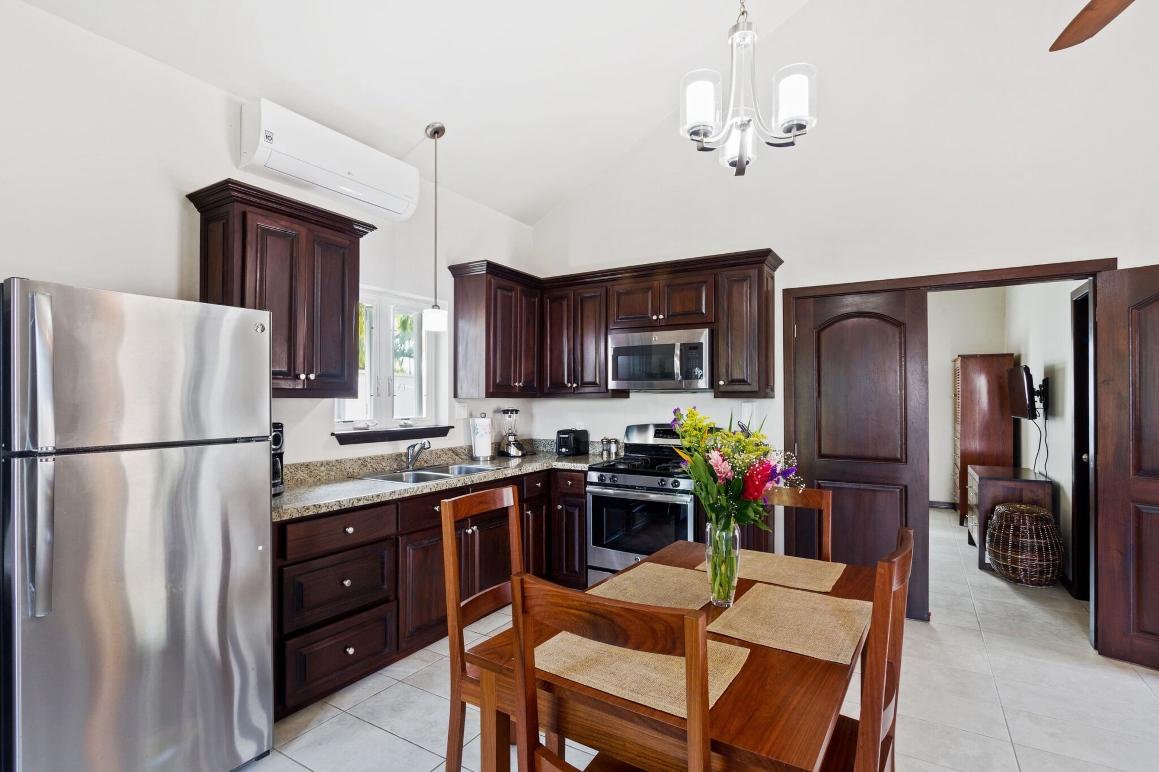 A modern kitchen with dark wooden cabinets, stainless steel appliances, and a dining area with a wooden table and chairs.